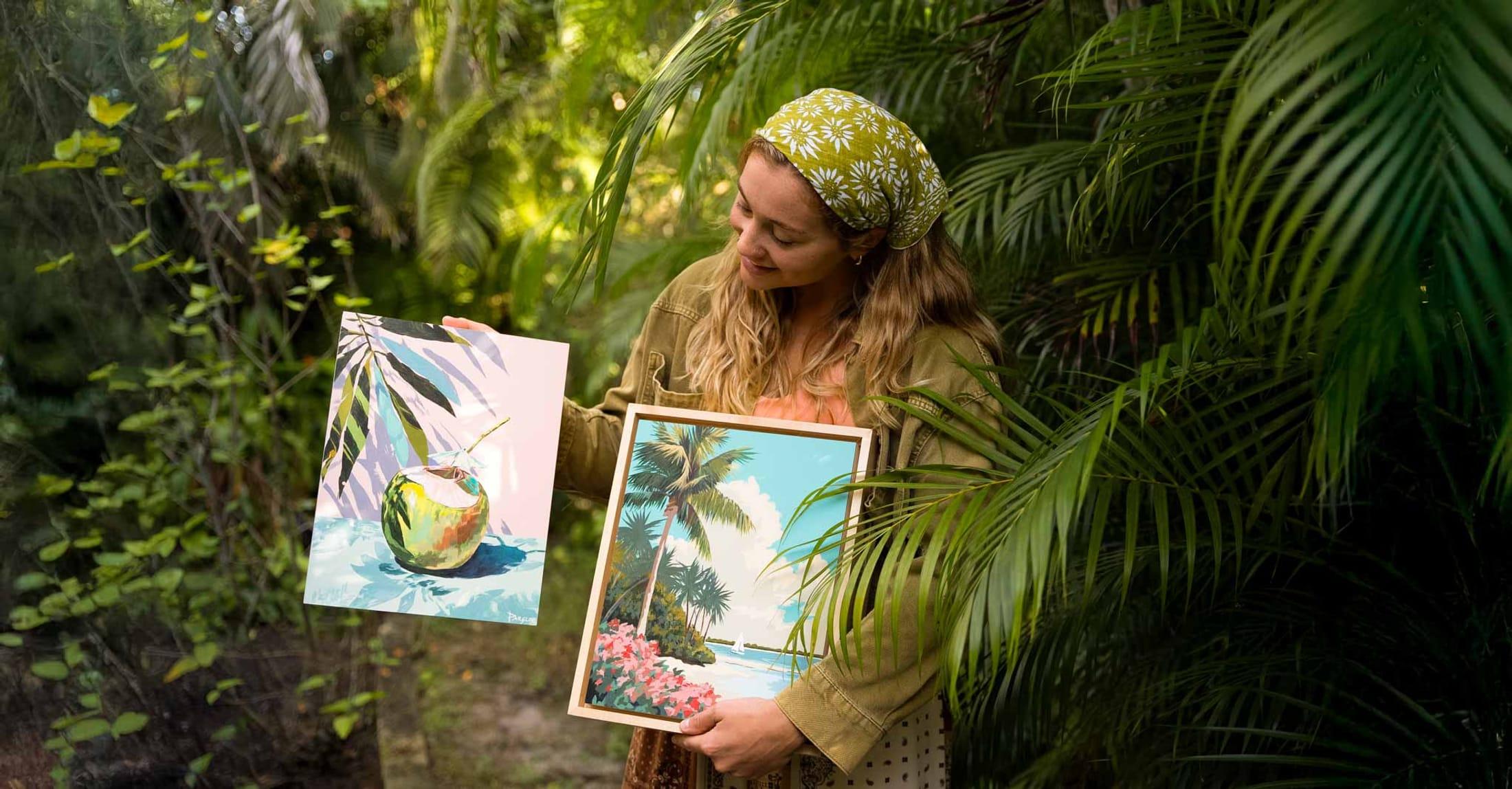 Tori holding two framed original paintings in the garden