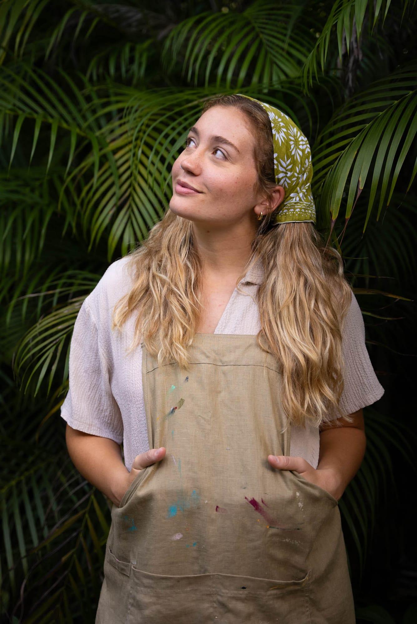 Portrait of Tori in her paint-splattered apron among palm leaves